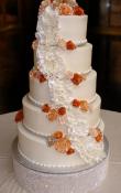 Candlelight buttercream iced,  5 tier round wedding cake decorated with fondant ruffles (matte and pearlescent).  Gumpaste Flowers as the topper. Rhinestone cake base.  (This cake can serve receptions with 250-380 expected guests)